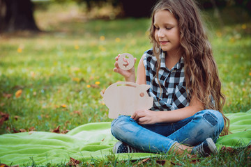 Little girl putting coin in piggy bank. Concept. Outdoors.