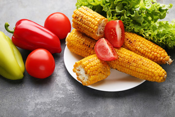 Fototapeta na wymiar Tasty grilled corns with vegetables on grey wooden table