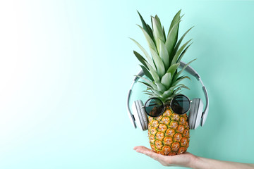 Female hand holding pineapple with sunglasses and headphones on mint background
