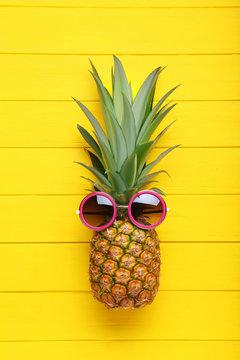 Ripe pineapple with sunglasses on yellow wooden table