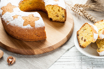 homemade traditional fruit cake slices on stand decorated with nuts and wheat ears at white wooden table