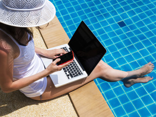 Young woman working with laptop and smartphone at poolside