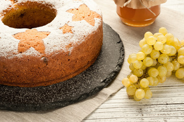 homemade traditional fruit cake on stone stand decorated with grapes and honey jar at white wooden table