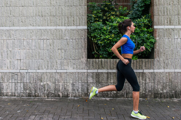 Profile view of a sporty young woman working out outdoors. Fitness girl running on sidewalk.
