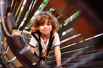 child - a cute, curly-haired boy in an amusement park climbing the rope road. Hyperactive child