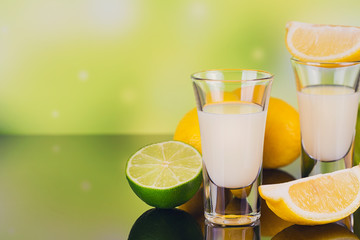 Glasses of cream liqueur with lime and lemon on green background with reflection.