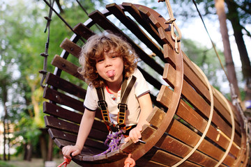 child - a cute, curly-haired boy in an amusement park climbing the rope road. Hyperactive child