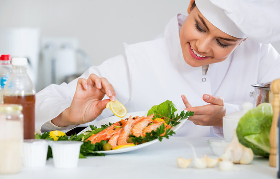 Young positive chef arranging cooked shrimps