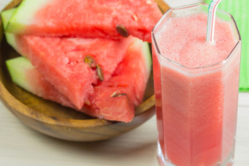 Watermelon juice in a glass glass with a straw on a light wooden background, a cocktail, a plate with slices of ripe berries watermelon
