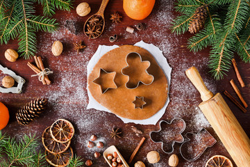Gingerbread cookies preparation. Christmas cookies baking on wooden background. Christmas decorations, gingerbread cookie dough, cookie cutters, spices, oranges and fir tree frame. Top view