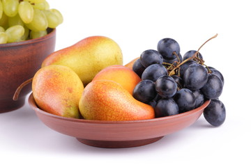 Yellow pears, green and blue grapes in a clay plate on a white background