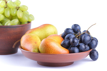 Yellow pears, green and blue grapes in a clay plate on a white background