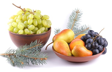 Yellow pears, green and blue grapes in a clay plate with Christmas tree branches on a Christmas dinner on a white background