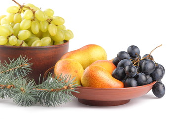 Yellow pears, green and blue grapes in a clay plate with Christmas tree branches on a Christmas dinner on a white background