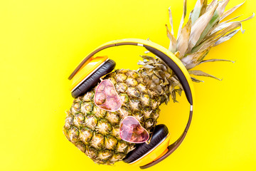 Pineapple-hipster in pink glasses and headpones on yellow background top view