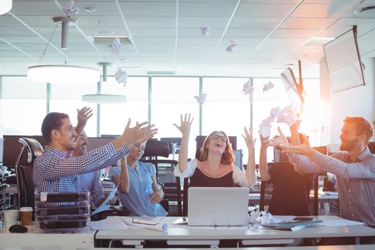 Cheerful Business People Tossing Crumpled Paper Balls At Desk In