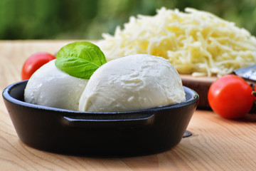 Mozzarella cheese balls in bowl and grated mozzarella with cherry tomatoes