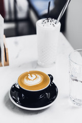 Cappuccino in black cup on white table