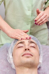 Cosmetician applying facial cream. Face of young man, cosmetology.