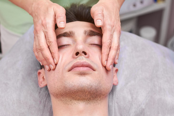 Fototapeta na wymiar Handsome guy, face massage. Hands of a masseuse working.