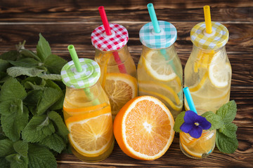 Fototapeta na wymiar bottles of water with citrus (orange and lemon) on a wooden table on a background of mint