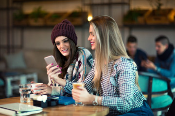 Two friends enjoying coffee together in a coffee shop and using phone