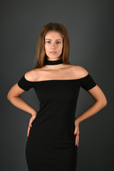 Young brunette lady in black dress posing on grey background