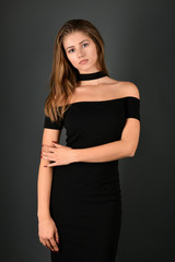 Young brunette lady in black dress posing on grey background