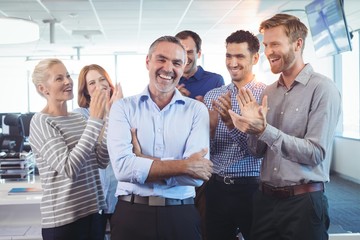 Happy businessman standing with arms crossed while colleagues