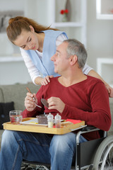 carer serving meal to man in wheelchair at home