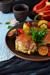 A hearty meal. Chicken thighs baked with potatoes, peppers and aubergines on a blue concrete background