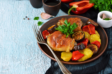 A hearty meal. Chicken thighs baked with potatoes, peppers and aubergines on a blue concrete background
