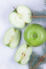 Whole and sliced green apples and a pink flower with branches of Christmas tree on a marble background for Christmas