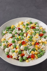 Frozen vegetables: corn, peas, tomatoes, carrots with rice on a plate.