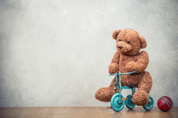Teddy Bear riding retro toy trike and old leather ball front concrete wall background. Vintage style filtered photo