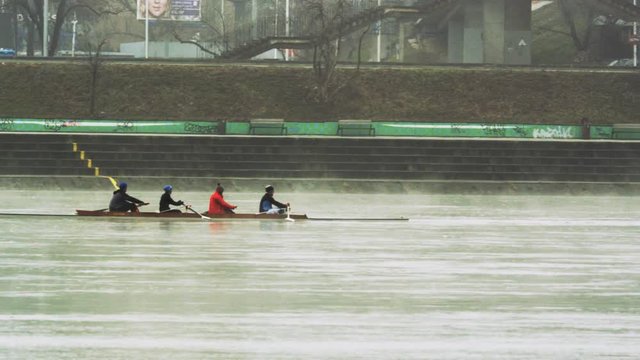 Rowing Four Moving Backwards on the River. Urban Area