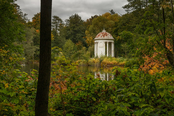 Classical white rotunda on the shore of a pond. Autumn Park. An ancient graceful rotunda with...