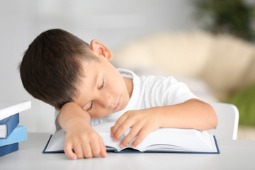 Naklejka premium Cute little boy sleeping while sitting at table with book