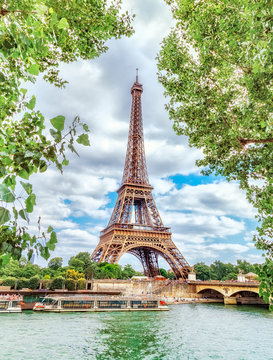 Classic view on Eiffel Tower through green poplar foliage over Seine river in Paris. Beautiful summer morning scenery. Vertical orientation. Eiffel Tower is famous travel destination in Europe.