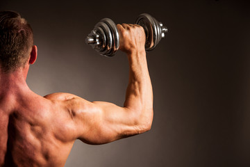 Fototapeta na wymiar Strong male athlete works out with dumbbells in studio over dark backgound