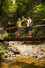 active young cople hiking on a wooden brifge over mountain creek