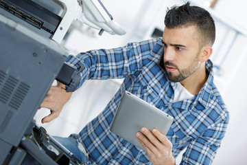 Obraz premium man leaning over open photocopier during maintenance repairs