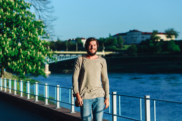Fototapeta premium Cheerful smiling young man posing on the embankment in the springtime