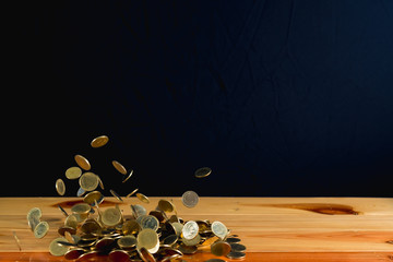 Falling gold coins money on wooden table with black wall, copy space, business wealth concept.