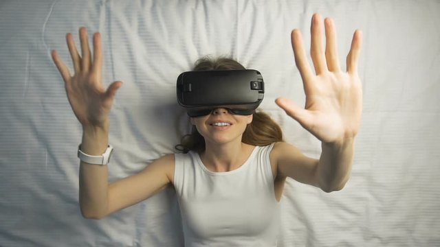 Dark hair caucasian girl sets her virtual reality helm, while enjoys using it on the huge white bed, slow motion
