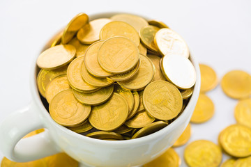 Golden coins in white cup of coffee on the white background.