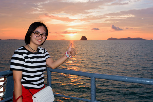 Women raise their thumb to admire the beautiful nature of colorful sky and sun at sunset over the sea on the deck of a passenger boat while cruising to Koh Samui Island in Surat Thani, Thailand
