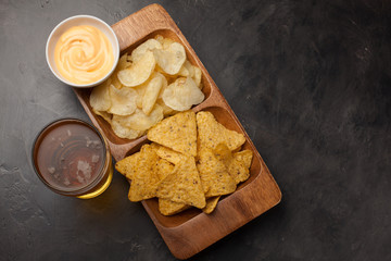 Beer in glasses closeup on the concrete table. Beer and snacks are chips and nachos in wooden bowl with cheese souce. top view. Copy space. Drink and snack for the football match or party