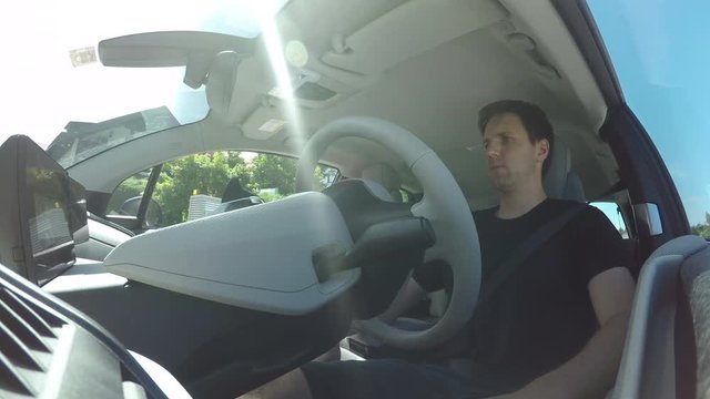 CLOSE UP: Man in innovative autonomous automated electric car using self-parking autopilot for parallel parking on street. Computer in autopilot mode turning wheel, moving vehicle on parking spot