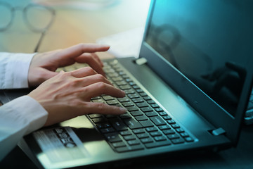 Side view of female hands typing on laptop keyboard.
